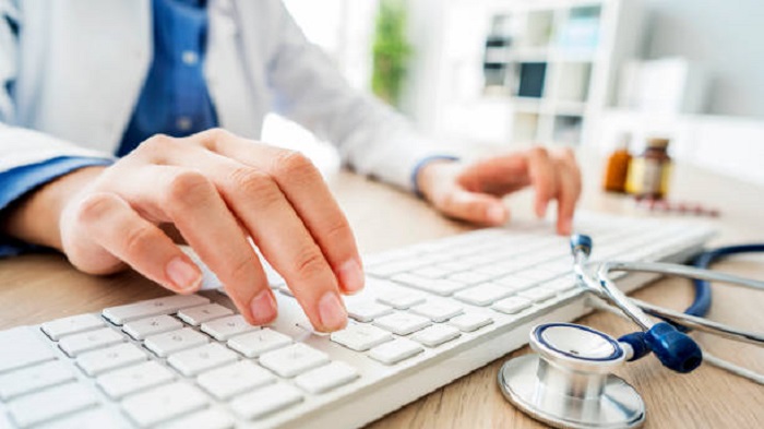 les mains d'une femme tapant sur le clavier d'un ordinateur à côté d'un stéthoscope - télésecrétaire médicale dédiée - Serenity